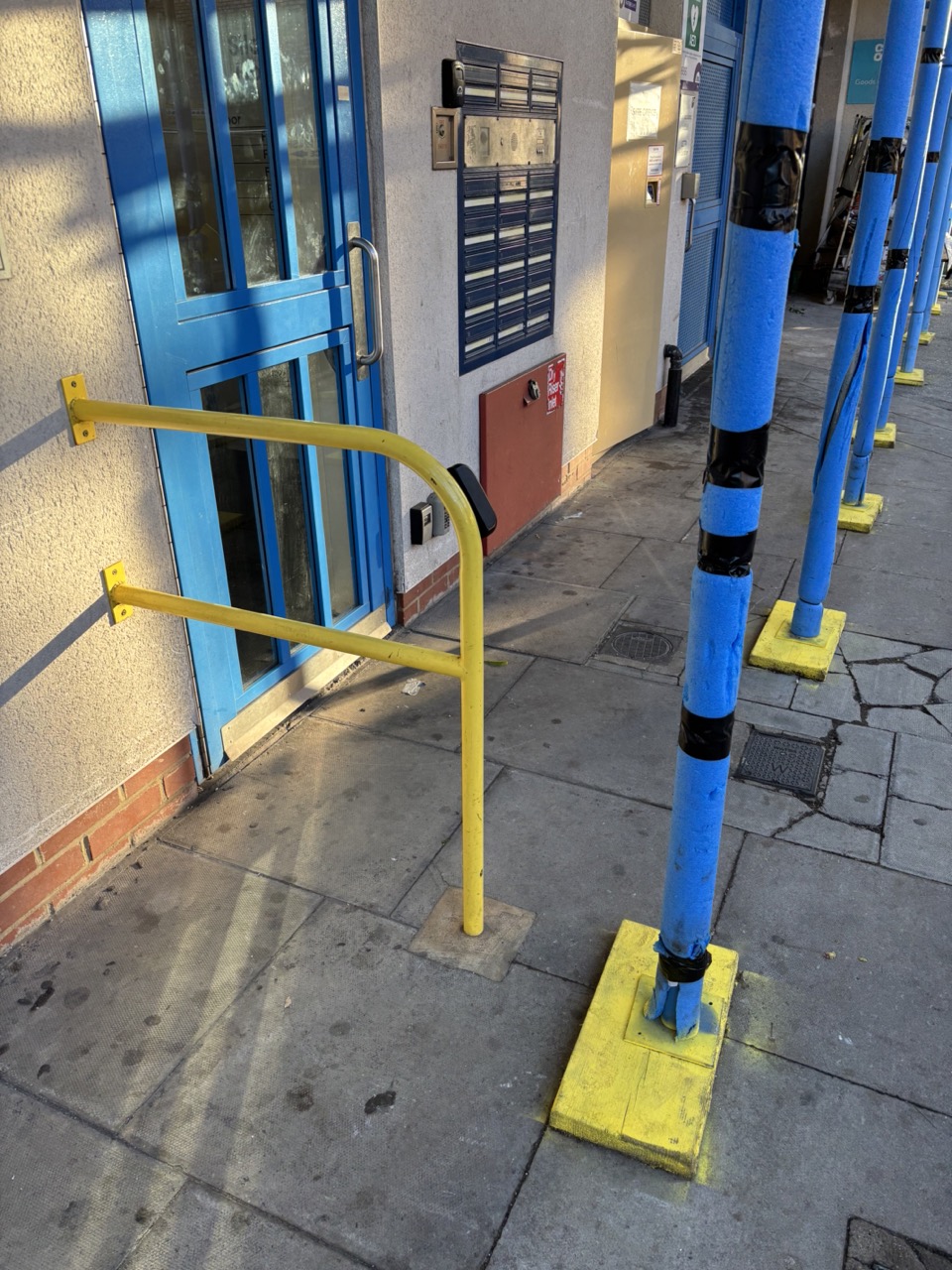 Scaffolding protection in blue and yellow coincidentally colour matching a building door and grab rail
